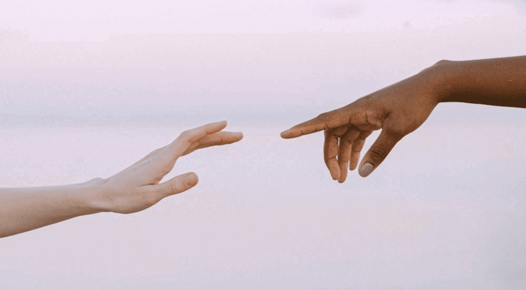 Two hands reaching out to each other in front of pink sky